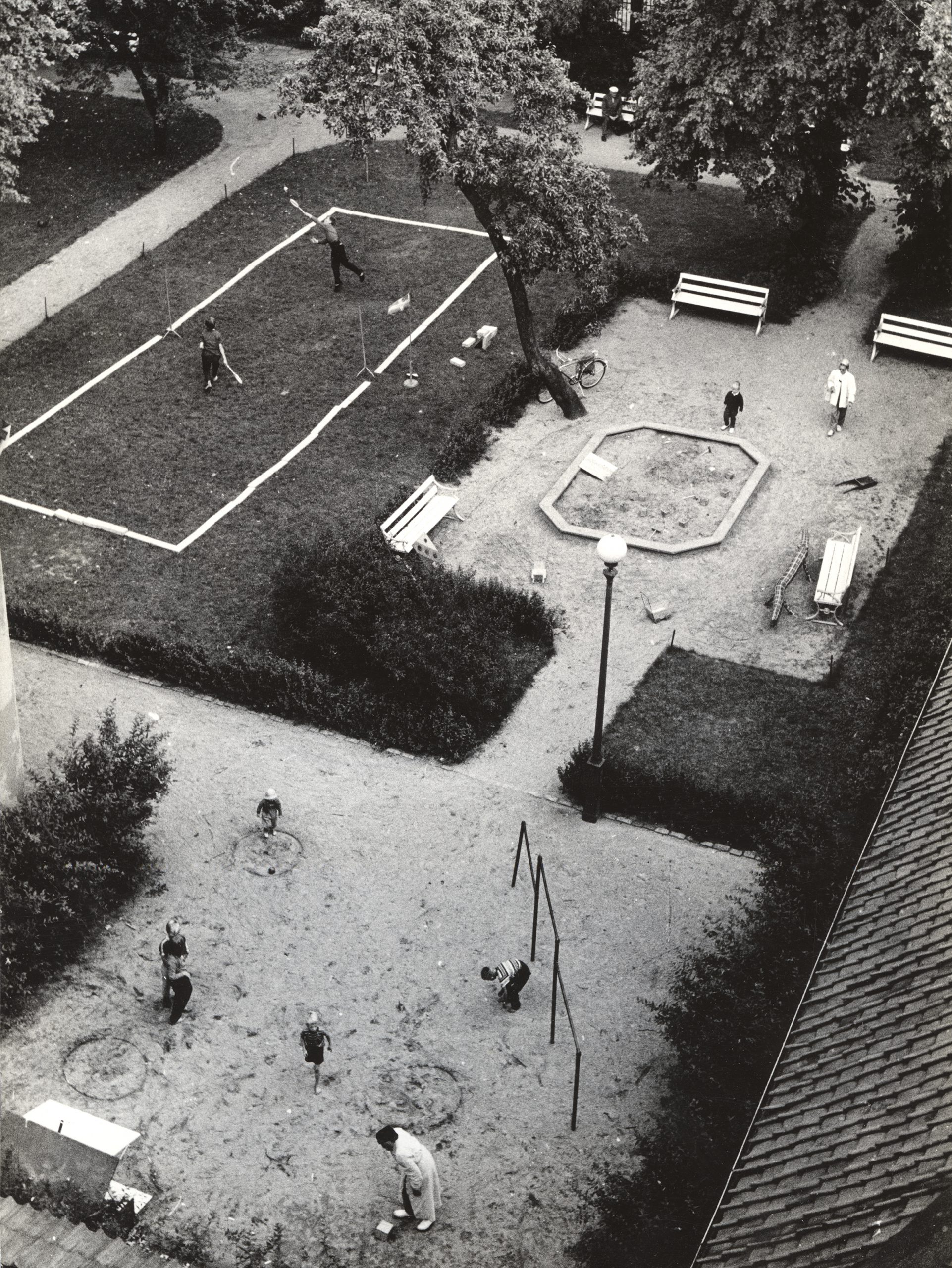 Översikt över Kronhusparken där två pojkar spelar badminton och en mamma med barn står vid en sandlåda.