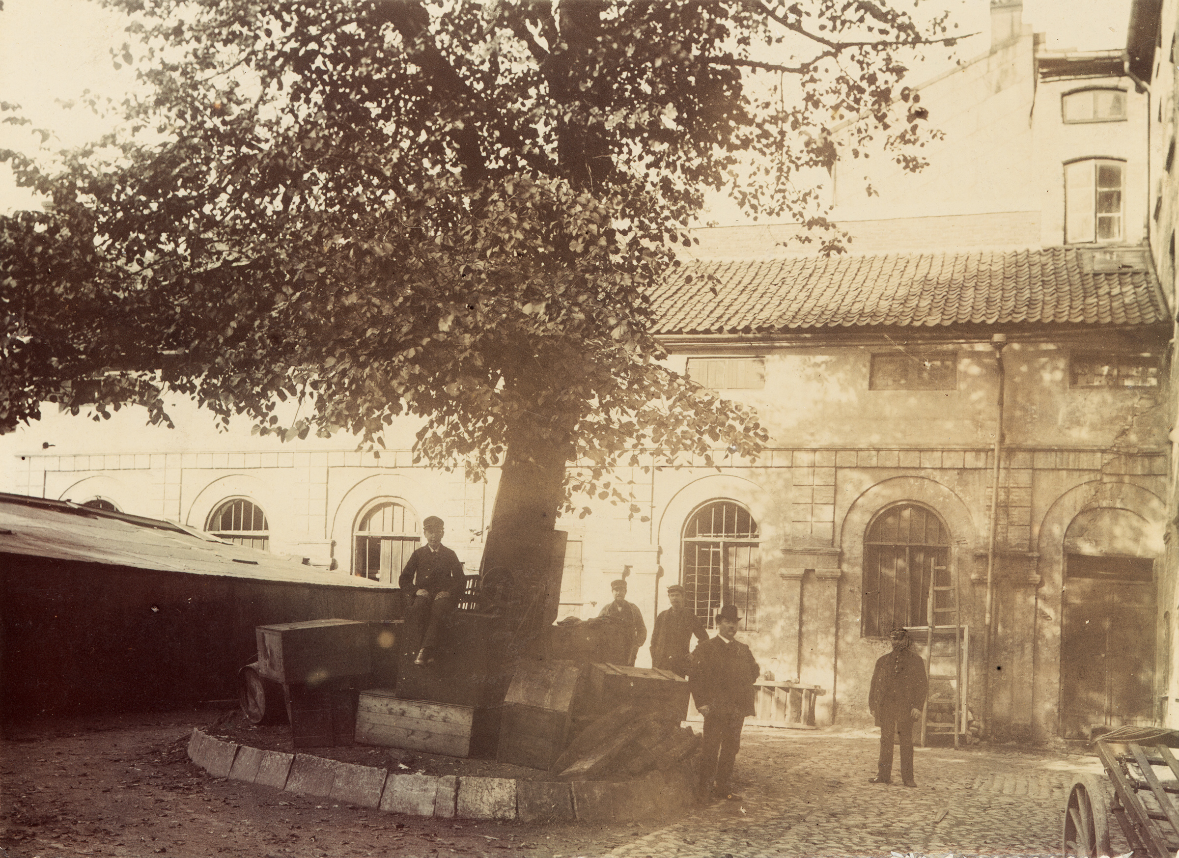 Fyra män står och en man sitter under ett träd på Hallska teaterns innergård.